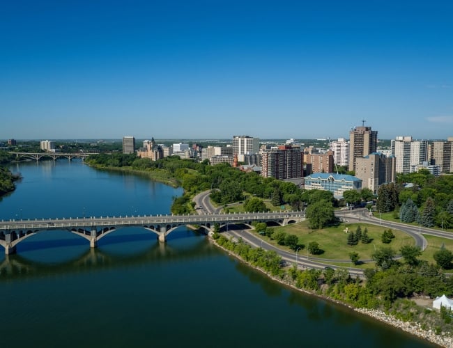 areal view of the Saskatoon city skyline, with a park and bridge in the foreground