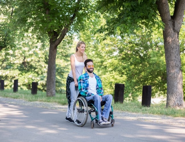 A women pushing a man in a wheelchair in a beautiful park