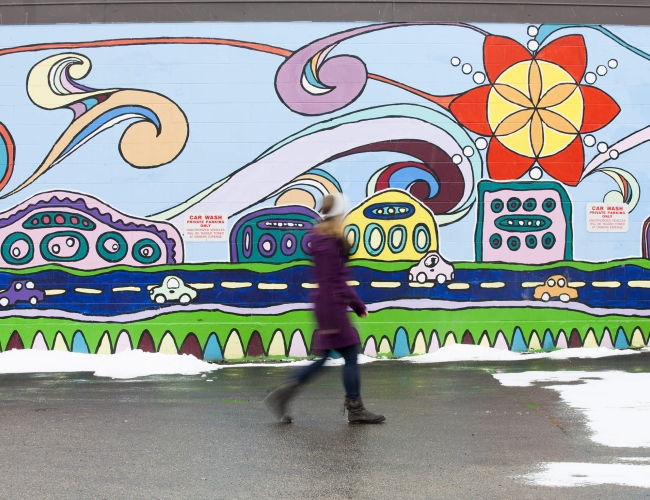 a woman dressed in a winter coat walking in front of a colourful mural